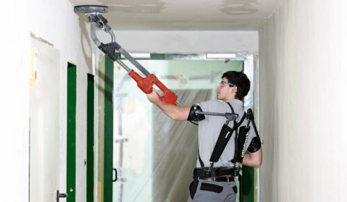 Das Exoskelett Paexo von Ottobock unterstützt Handwerker auf Baustellen bei der Überkopfarbeit, zum Beispiel beim Schleifen der Decke mit einer „Giraffe“ (Teleskopschleifer). (Foto: Ottobock)