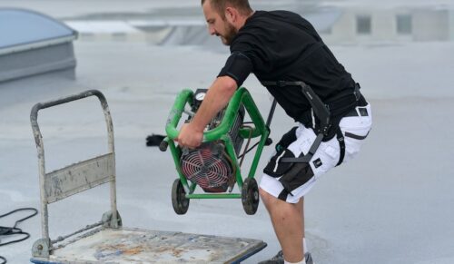 Ein Mitarbeiter von Schühle Abdichtungen nutzt das Exoskelett IX Back Air zur Rückenentlastung beim Heben schwerer Lasten. (Foto: SUITX by Ottobock)