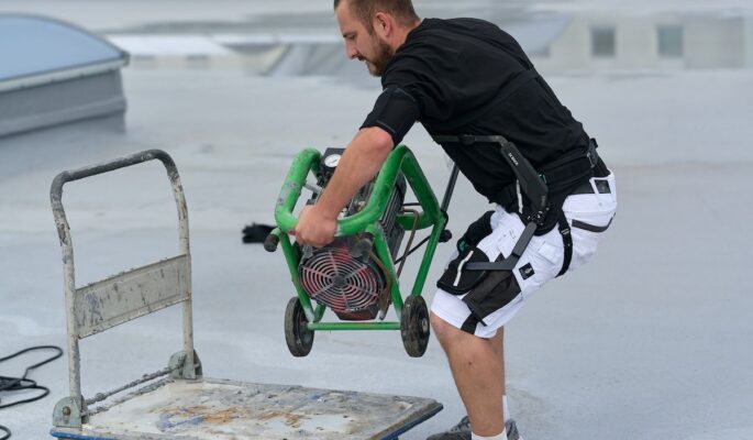 Ein Mitarbeiter von Schühle Abdichtungen nutzt das Exoskelett IX Back Air zur Rückenentlastung beim Heben schwerer Lasten. (Foto: SUITX by Ottobock)
